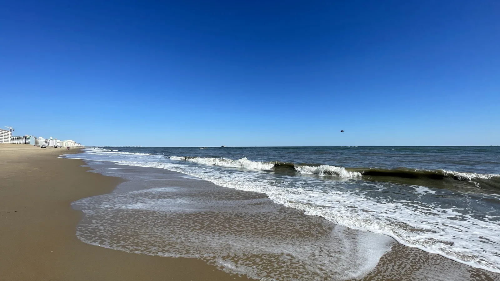 Waves on the beach at the Virginia Beach Oceanfront, with the hotels and the fishing pier in the distance.